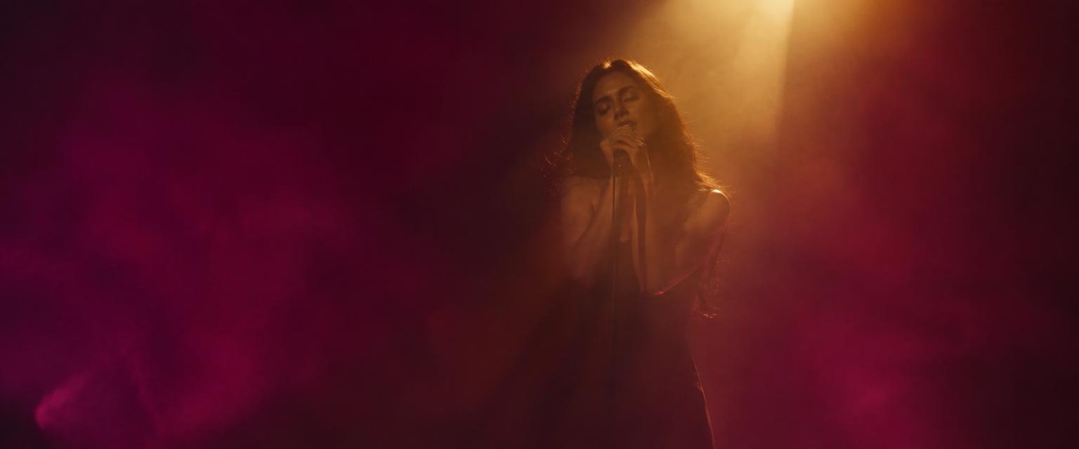 A singer performs under a single golden spotlight in plum-colored haze